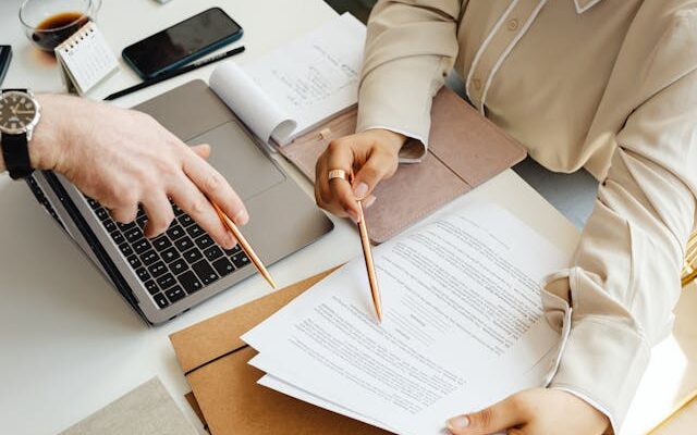two people working at desk with laptop and papers