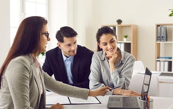 a-businesswoman-presenting-information-on-a-laptop-to-a-smiling-couple-in-an-office