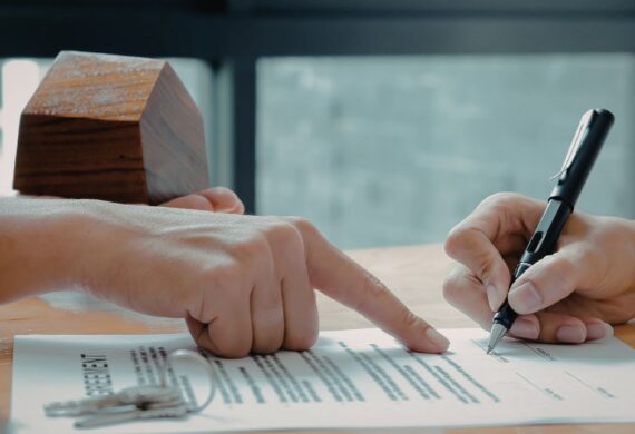 Person signing a lease or real estate agreement while another person points to the document